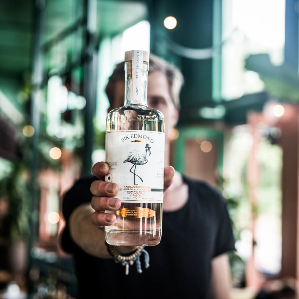A bottle of Sir Edmon Gin being presented with the surrounding environment blurred.