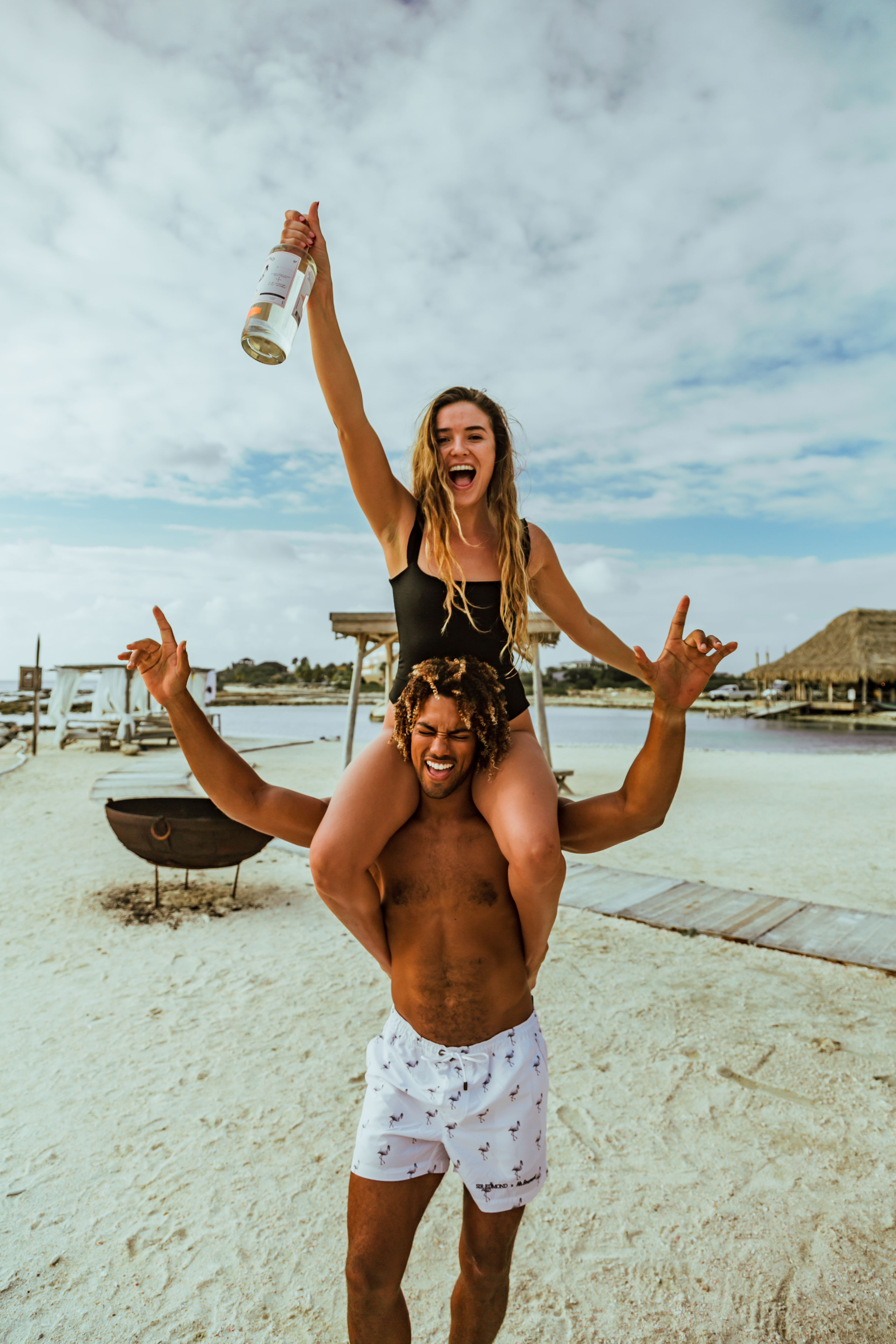 A branding image of a bottle of Sir Edmond gin on the beach being held by a woman.