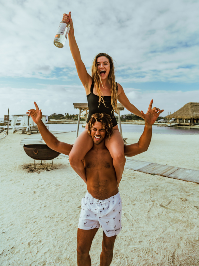A branding image of a bottle of Sir Edmond gin on the beach being held by a woman.
