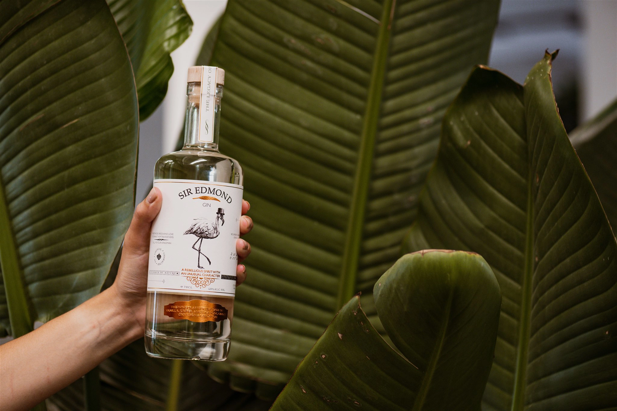 Image of a Sir Edmond bottle of gin being held above leaves.