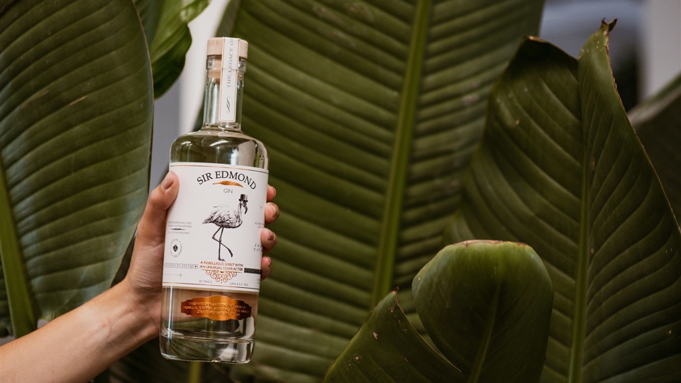 Image of a Sir Edmond bottle of gin being held above leaves.