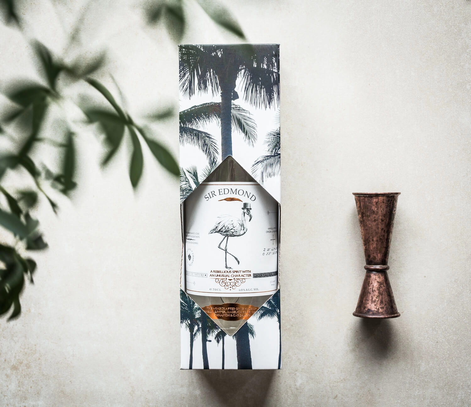 Bottle of Sir Edmond Gin in its packaging with a measuring cup besides.