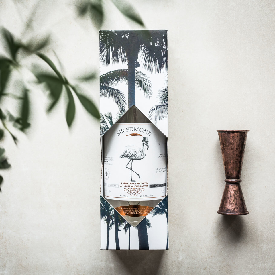 Bottle of Sir Edmond Gin in its packaging with a measuring cup besides.