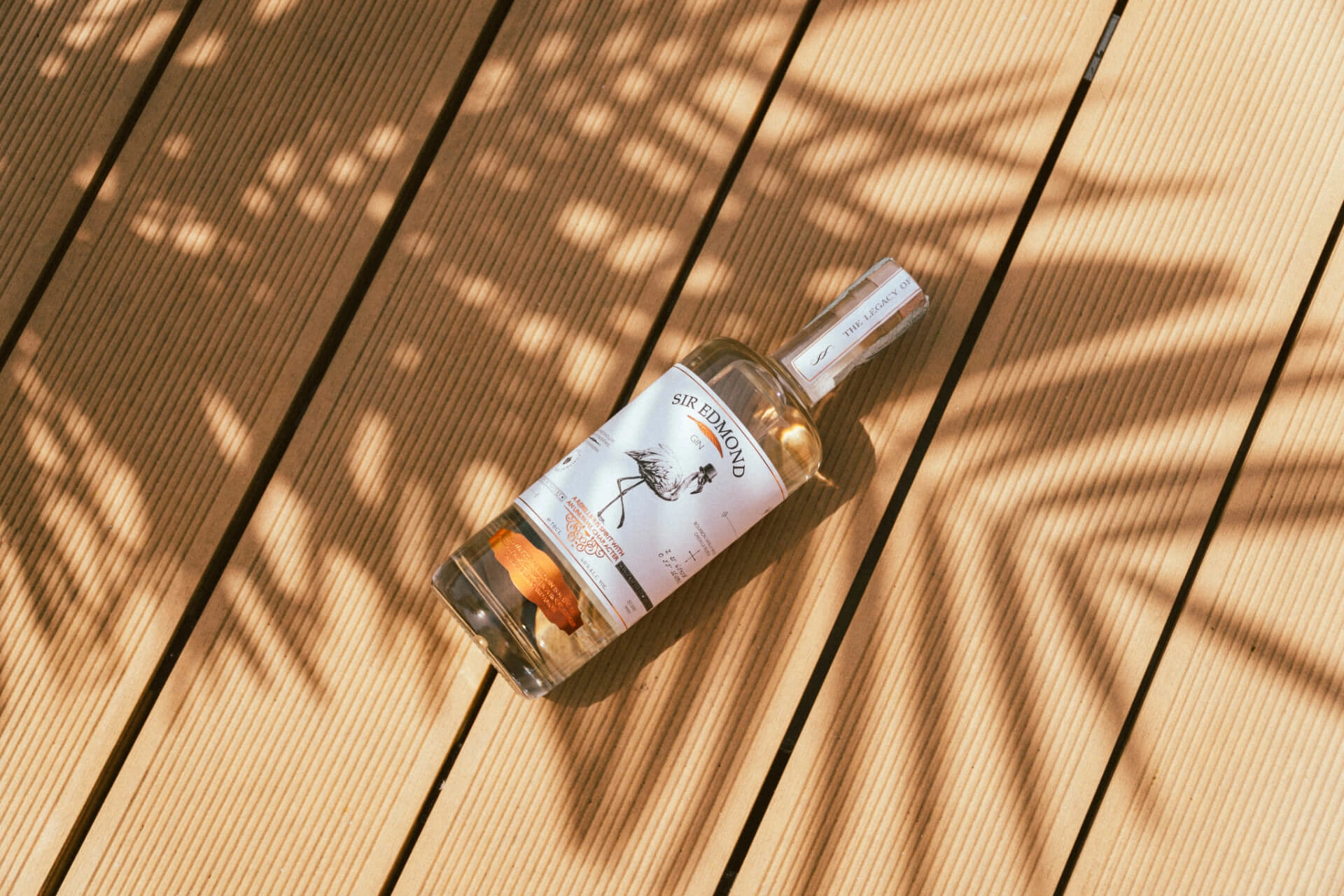 Bottle of Sir Edmond Gin laying on a wooden floor.